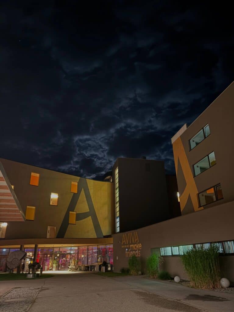 Stimmungsvoll beleuchtetes Eingangsportal des Lifestylehotels AVIVA bei Nacht mit warmen Goldakzenten.